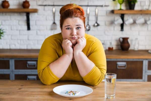 Mulher obesa, triste, frente a um prato cheio de medicações.