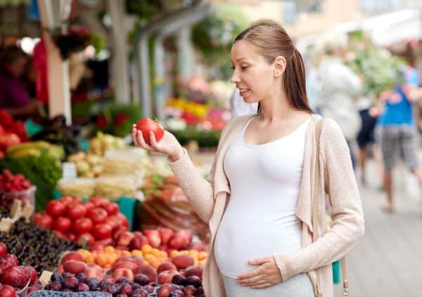 Mulher grávida escolhendo frutas e legumes numa feira.