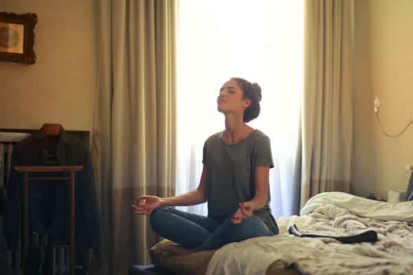 Estresse e meditação - mulher fazendo meditação em cima de sua cama.